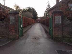 A straight road running between green gates and brick gate posts with plaques